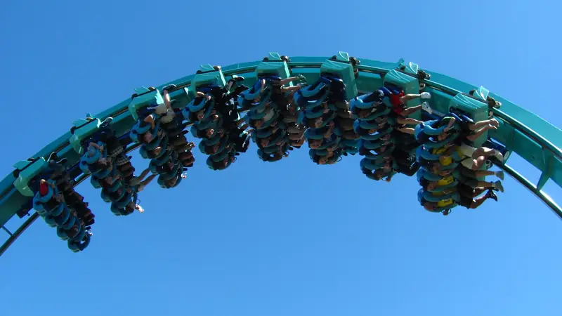 Riders on the teal Kraken roller coaster at SeaWorld Orlando against a blue sky